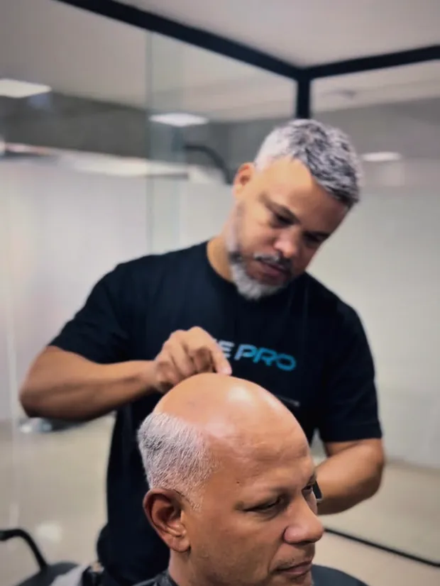 Barbeiro aplicando prótese capilar em um cliente no Studio Wolver